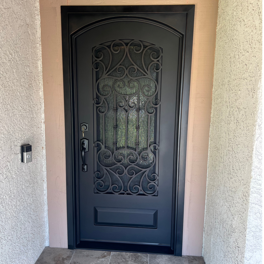 Black wrought iron door with decorative glass panel on a beige wall.