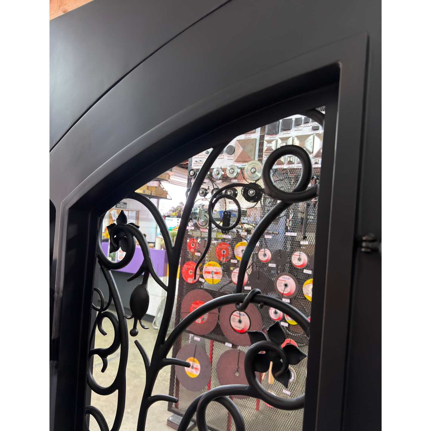 Decorative black metal gate with intricate designs, partially open, revealing a store interior with various items.
