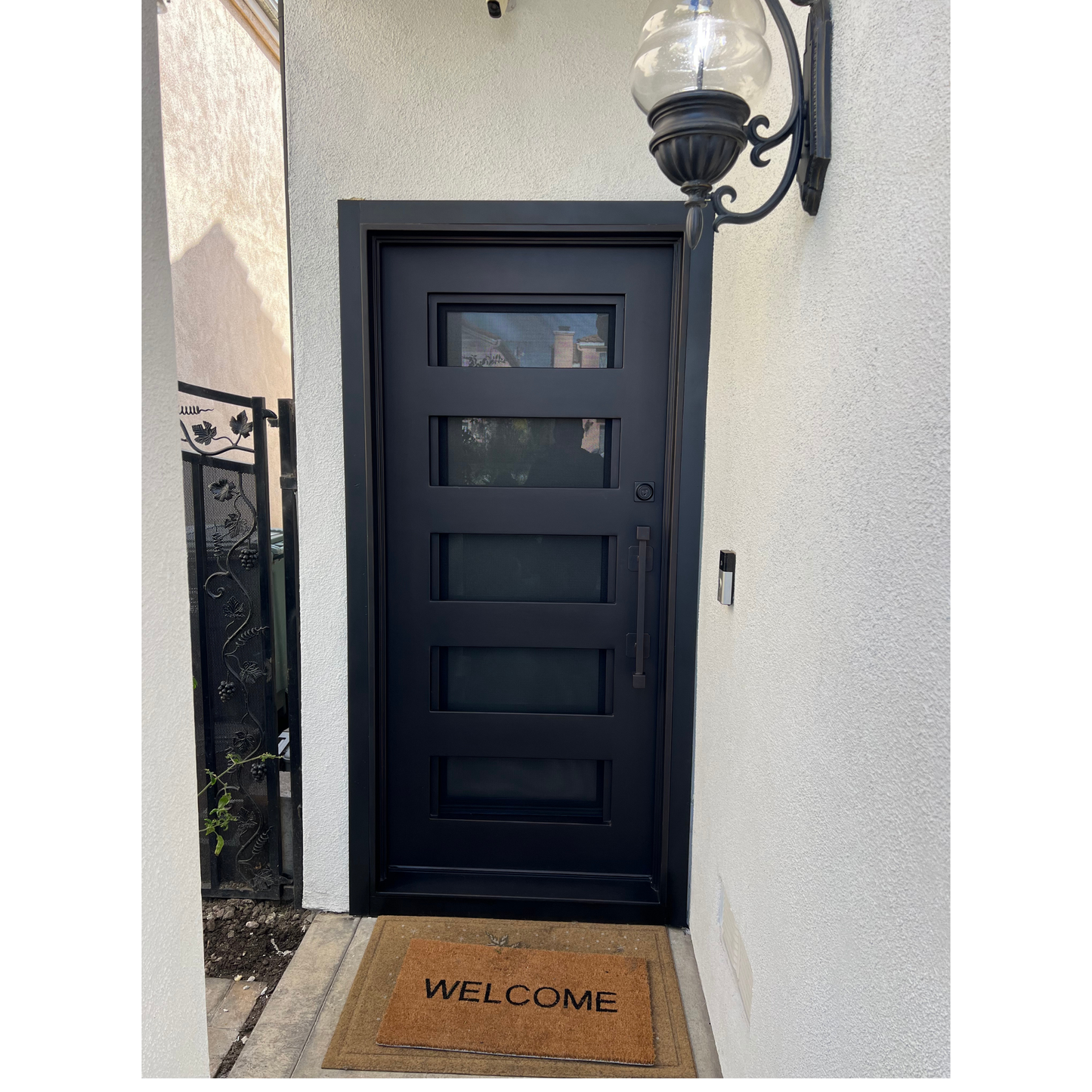 Black front door with a 'Welcome' mat on a white wall