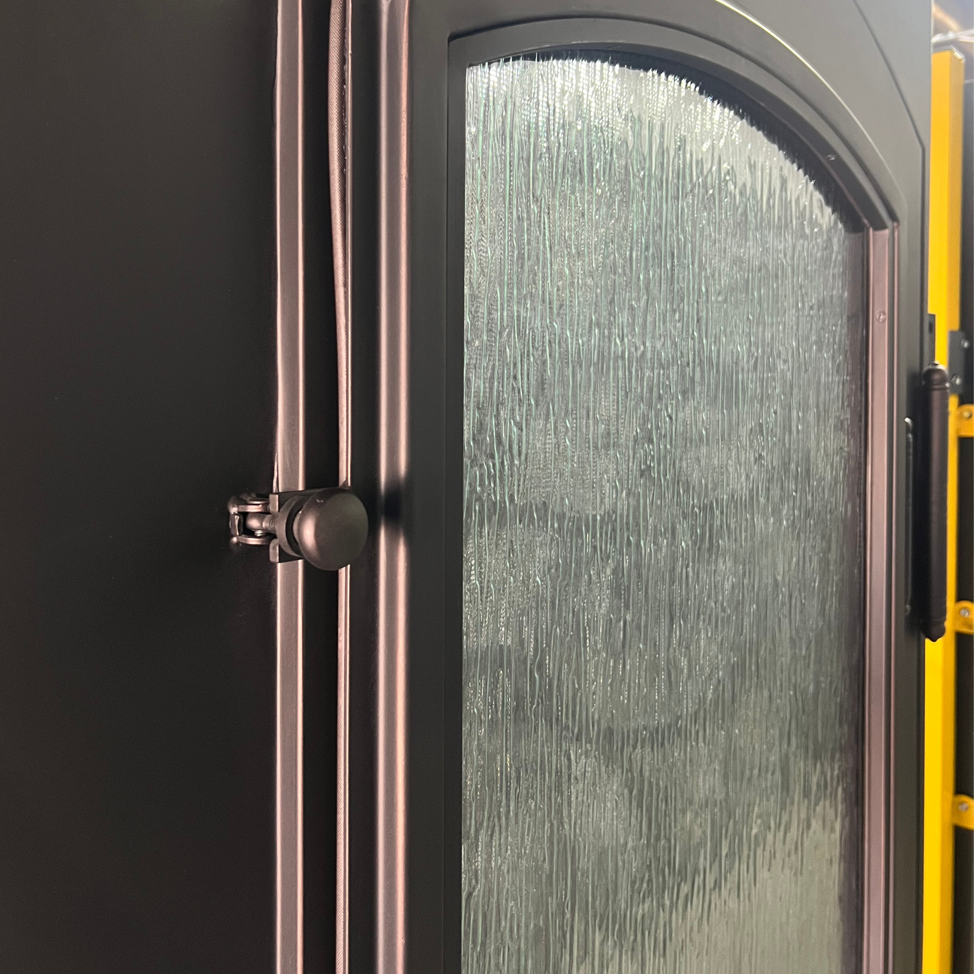 Close-up of a glass door with a metallic handle and yellow frame.